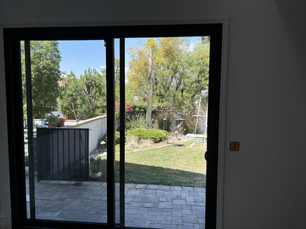 A view of a grassy backyard through an Anlin sliding glass door in a Designer Black™ finish.